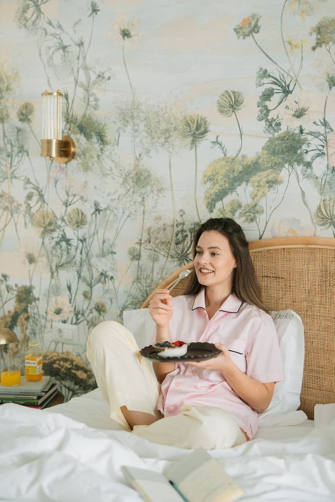 Femeie relaxată luând micul dejun în pat, savurând iaurt cu fructe și un suc natural Juiceit. Un început perfect al zilei, cu un stil de viață sănătos și echilibrat.