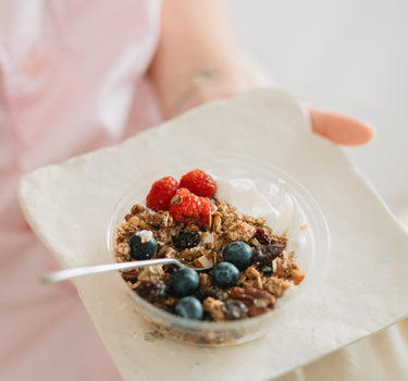 Mic dejun sănătos cu granola, fructe de pădure și iaurt, servit într-un bol transparent pe o farfurie albă, ideal pentru un start energic al zilei.