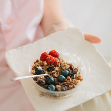 Mic dejun sănătos cu granola, fructe de pădure și iaurt, servit într-un bol transparent pe o farfurie albă, ideal pentru un start energic al zilei.
