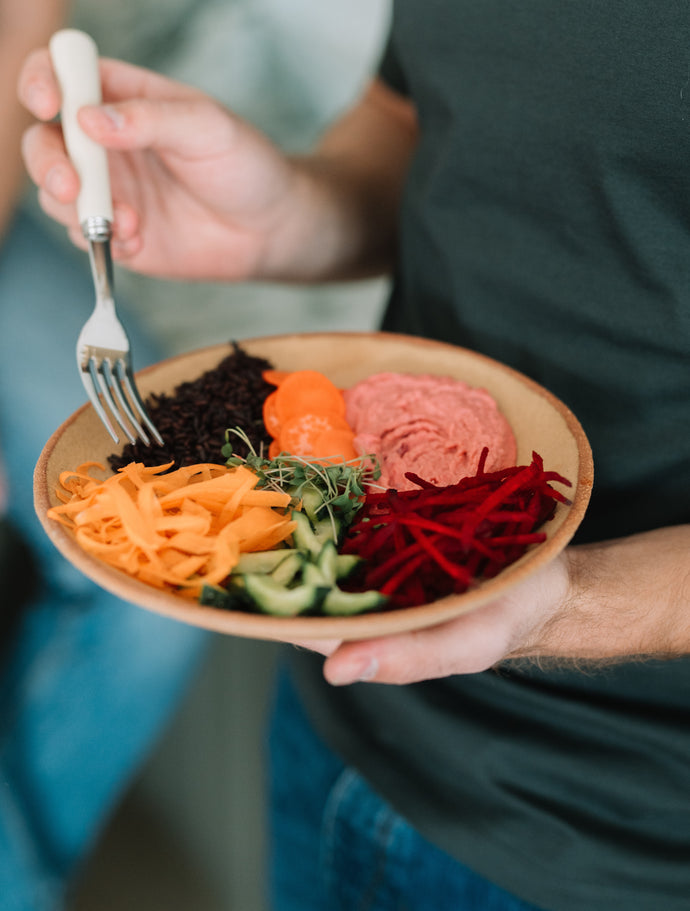 Bol vegetarian colorat cu ingrediente proaspete: morcovi, castraveți, sfeclă roșie, germeni și humus, perfect pentru un prânz nutritiv și echilibrat.