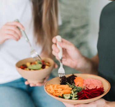 Două persoane savurând boluri sănătoase cu legume proaspete, orez negru, hummus și dressing natural, parte din programul de mese Plant Power de la Juiceit.