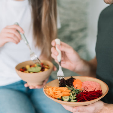 Două persoane savurând boluri sănătoase cu legume proaspete, orez negru, hummus și dressing natural, parte din programul de mese Plant Power de la Juiceit.