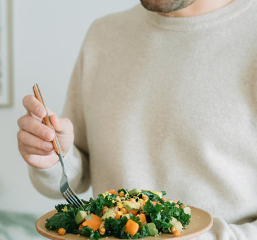 Bărbat savurând o salată sănătoasă cu kale, năut crocant, avocado și dovleac, perfectă pentru un prânz nutritiv și echilibrat.