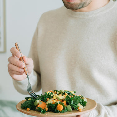 Bărbat savurând o salată sănătoasă cu kale, năut crocant, avocado și dovleac, perfectă pentru un prânz nutritiv și echilibrat.